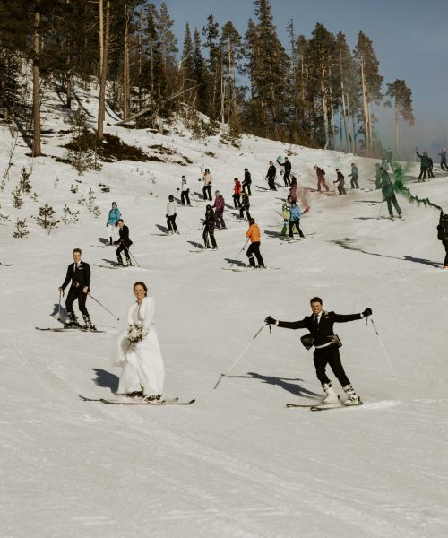 Bröllopsgäster och brudpar åker skidor nerför backe i fjällen